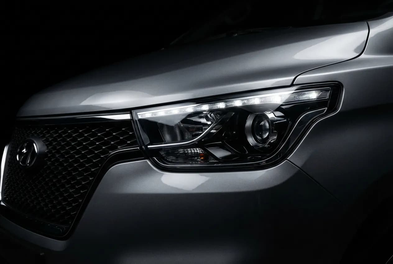 Hyundai H1 4x4 Starex : Avis, Fiche Technique et Prix Gros plan iconique et contrasté sur le phare d'un van Hyundai H1 4x4 Starex sur un fond noir uni.